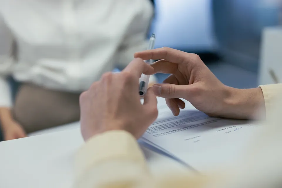 Two people talking across a table, one holding a pen over a document.